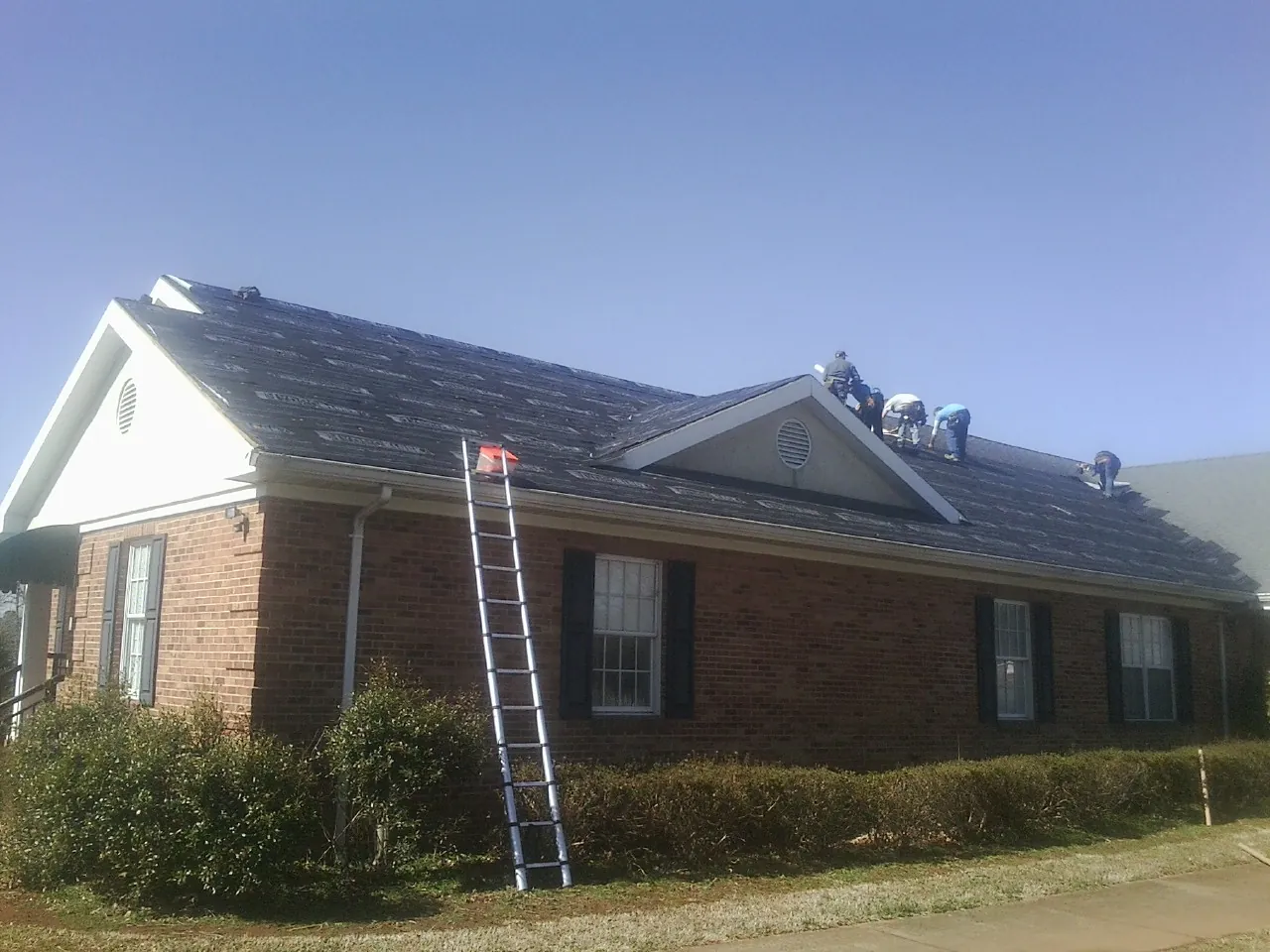 Crew tearing shingles off a brick ranch roof with a ladder set — Emergency Roof Repair work by our crew in Pinecliffe