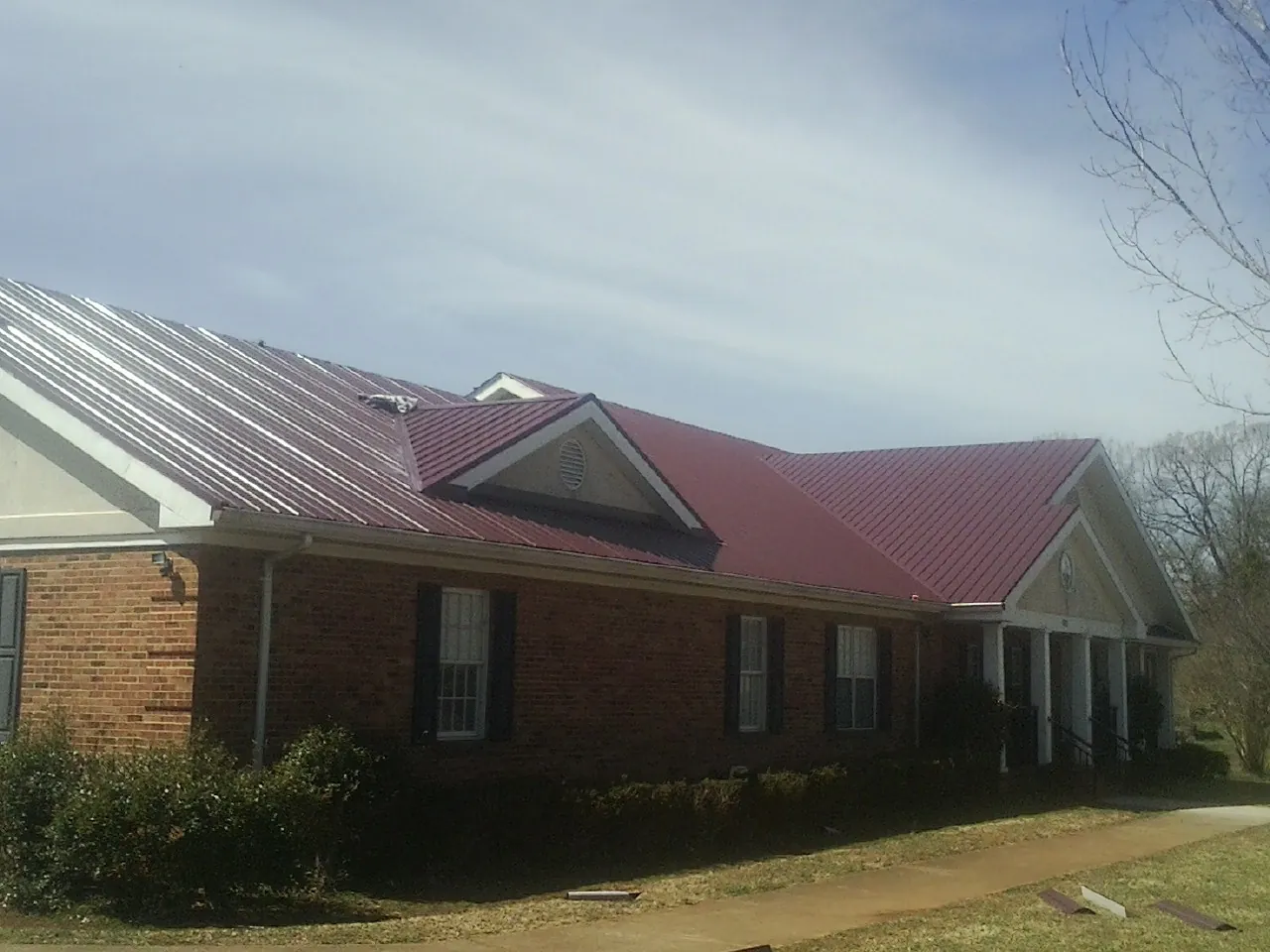 Red metal roof with gabled entries on a long brick building, from a Hail Damage Roof Repair job in Pinecliffe