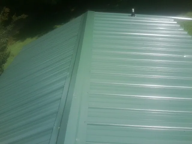 New green metal panels meeting at the ridge of a roof — Flat Roof Repair work by our crew in Pinecliffe