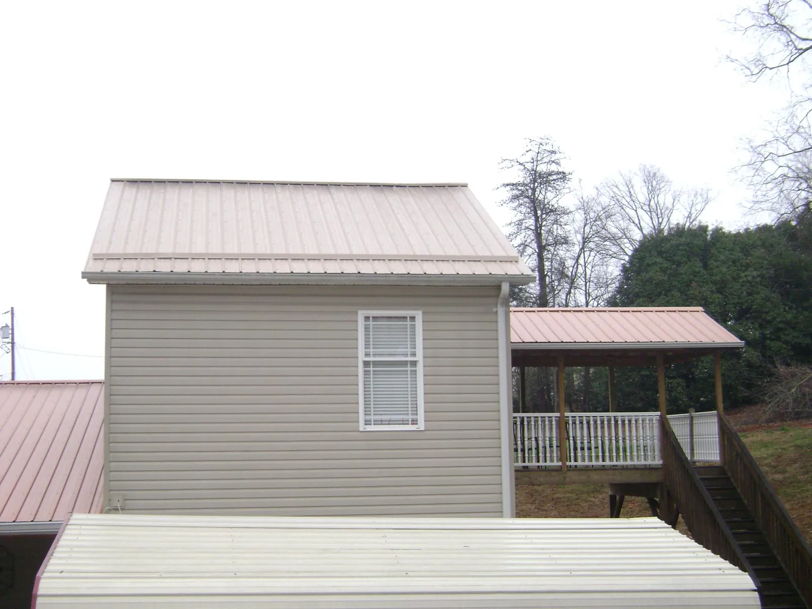 Tan metal roofs on a two story addition and attached porch, from a Roof Replacement job in Pinecliffe